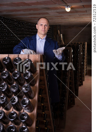 Male inspecting wine bottles in wine cellar Male inspecting wine bottles in wine cellar 72812519