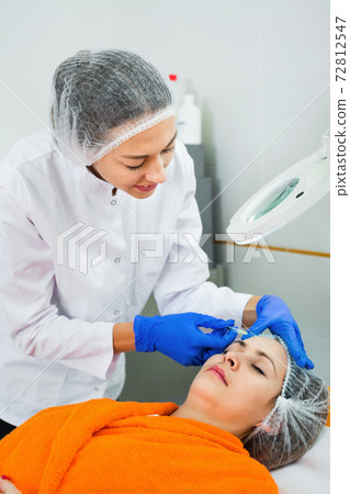 Woman doctor making beauty injection to young female client Woman doctor making beauty injection to young female client 72812547