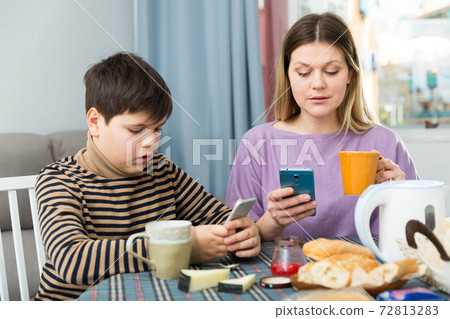 Portrait of young woman and using phones during breakfast at table Portrait of young woman and using phones during breakfast at table 72813283