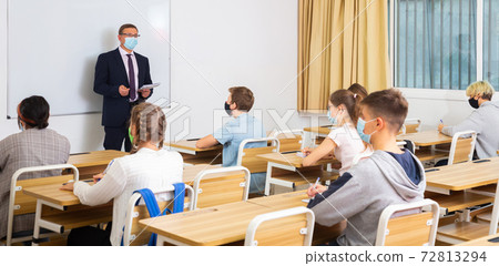 Teacher in protective mask is giving lecture for students in class Teacher in protective mask is giving lecture for students in class 72813294