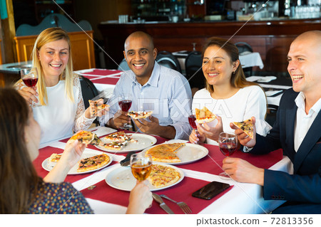 Cheerful young adults enjoying pizza in cozy restaurant Cheerful young adults enjoying pizza in cozy restaurant 72813356