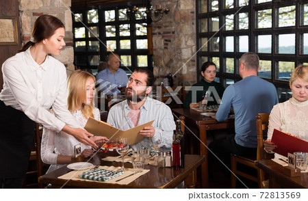 Guests of the country restaurant discuss menu with waitress Guests of the country restaurant discuss menu with waitress 72813569