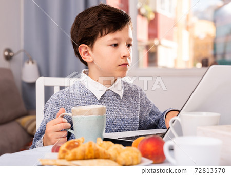 Teenager plays on laptop in kitchen interior 72813570