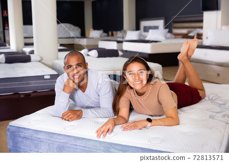 Cheerful loving Hispanic couple lying on new modern orthopedic mattress in furniture shop trying its comfort and convenience Cheerful loving Hispanic couple lying on new modern orthopedic mattress in furniture shop trying its comfort and convenience 72813571