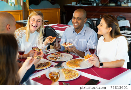 Cheerful friends enjoying dinner with pizza in cozy restaurant Cheerful friends enjoying dinner with pizza in cozy restaurant 72813601