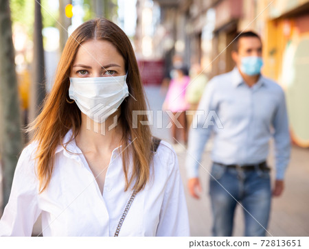 Young woman in medical mask walking along city street Young woman in medical mask walking along city street 72813651