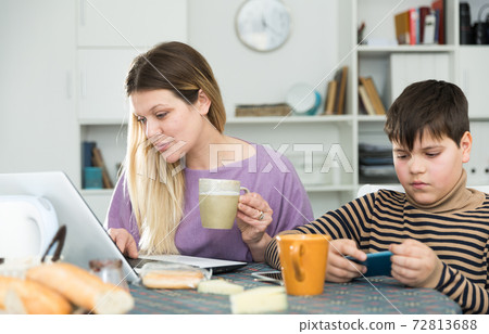Portrait of young mother and son with tea using gadgets at table Portrait of young mother and son with tea using gadgets at table 72813688