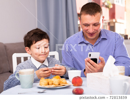 Cheerful man and his son with smartphones Cheerful man and his son with smartphones 72813839
