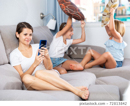 Woman using phone while daughters pillow fighting Woman using phone while daughters pillow fighting 72813842