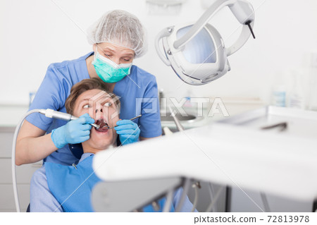 Male patient sitting on chair in dental office getting dentist treatment Male patient sitting on chair in dental office getting dentist treatment 72813978