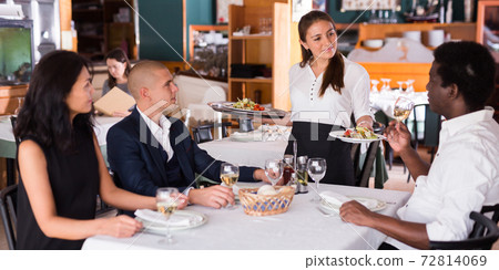 Young hispanic waitress serving meals to company in restaurant Young hispanic waitress serving meals to company in restaurant 72814069