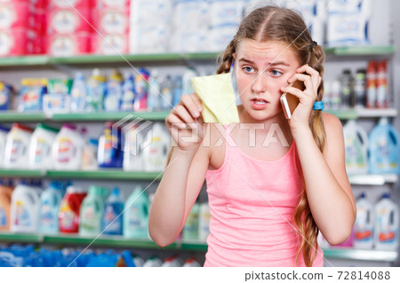 concentrated girl standing in store choosing products while talking by phone and looking at shopping list 72814088