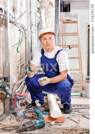 Experienced electrician laying electric wires in building under construction Experienced electrician laying electric wires in building under construction 72814179
