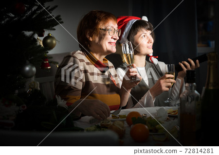Happy mother and daughter drink champagne and watch TV on Christmas night Happy mother and daughter drink champagne and watch TV on Christmas night 72814281