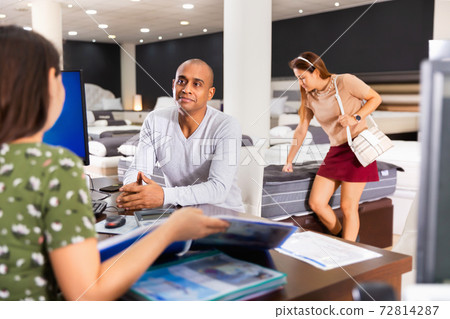 Positive latin american man visiting furniture store in search of comfortable mattress, talking to saleswoman Positive latin american man visiting furniture store in search of comfortable mattress, talking to saleswoman 72814287