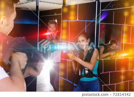 Laser tag players guys and girls playing in teams in dark laser Laser tag players guys and girls playing in teams in dark laser 72814342