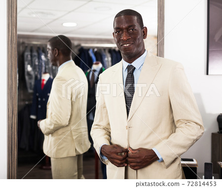 Confident male customer choosing fashion beige suit in mens store 72814453