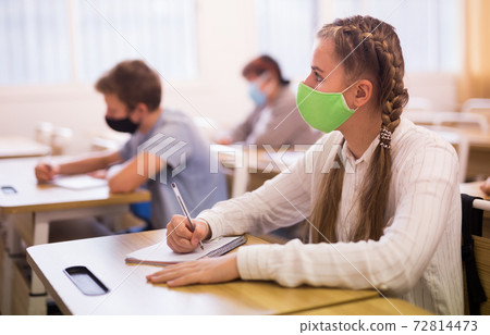 Schoolgirl wearing face mask working in class Schoolgirl wearing face mask working in class 72814473