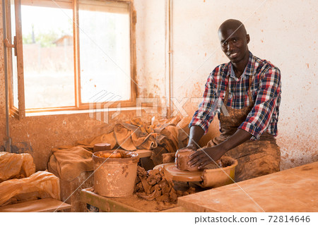 Smiling guy working with clay on potter wheel Smiling guy working with clay on potter wheel 72814646