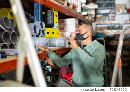 Latin american man in protective mask choosing plastic pipes in store Latin american man in protective mask choosing plastic pipes in store 72814912