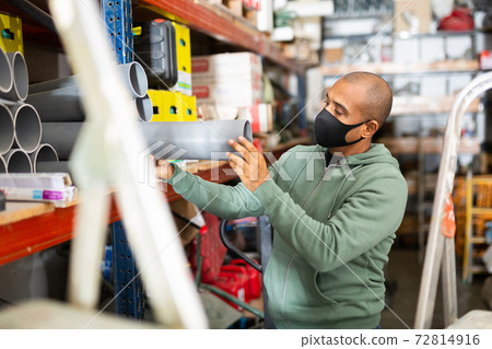 Craftsman in protective mask selects plastic plumbing pipes in hardware store 72814916