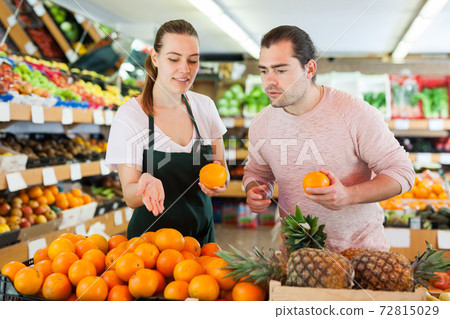 Young woman wearing apron selling fresh oranges to man customer Young woman wearing apron selling fresh oranges to man customer 72815029