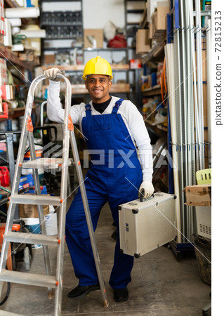 Portrait of worker in protective helmet and overalls with toolbox in hardware store Portrait of worker in protective helmet and overalls with toolbox in hardware store 72815213
