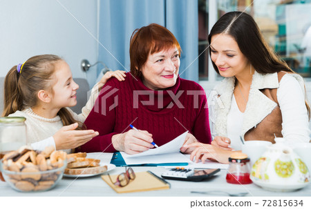 Smiling senior woman with family writing papers Smiling senior woman with family writing papers 72815634