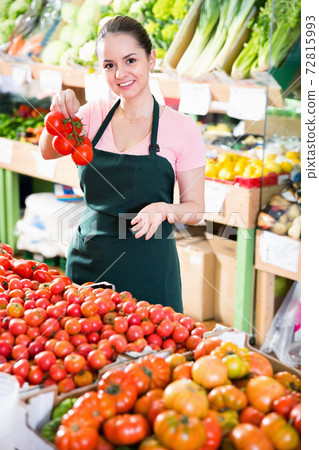 Positive female grocery worker in apron selling fresh red tomatoes 72815993