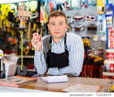 Man seller wearing uniform having tools in hands in store Man seller wearing uniform having tools in hands in store 72816074