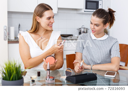 Smiling young girlfriend doing make-up at table in home 72816093