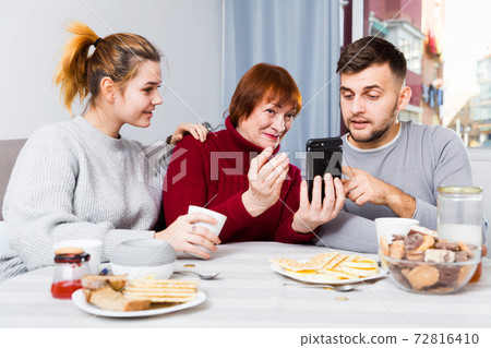 Senior woman with adult children using mobile gadget Senior woman with adult children using mobile gadget 72816410