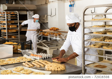 Male baker working with dough forming baguettes 72816508