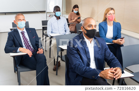 International group of business people in protective masks listening to presentation at tables 72816620