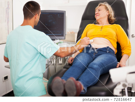 doctor examines a mature woman at abdomen with ultrasound doctor examines a mature woman at abdomen with ultrasound 72816647
