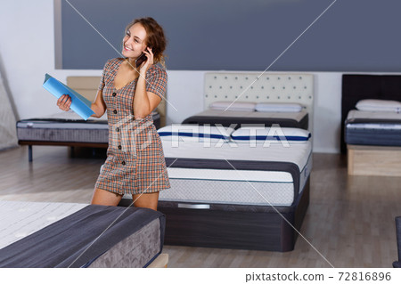 Young attractive woman talking on phone while choosing new mattress in home furnishings store 72816896