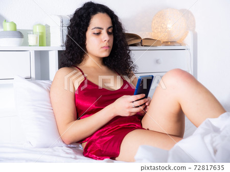 Woman using mobile phone lying on bed Woman using mobile phone lying on bed 72817635
