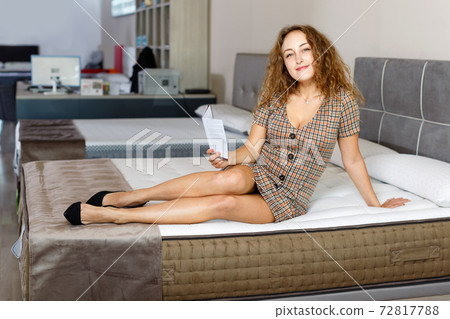 Young attractive woman choosing right mattress with booklet in home furnishings store 72817788
