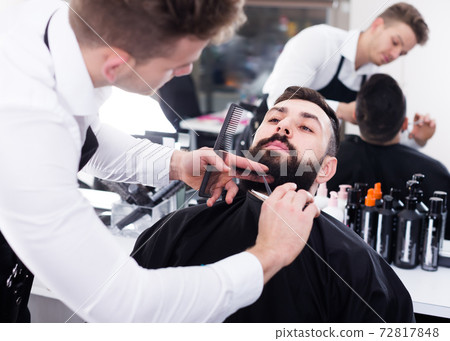 Ordinary man forming beard of client into shape 72817848