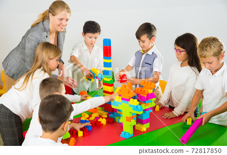 Kids and teacher playing with toy building blocks Kids and teacher playing with toy building blocks 72817850