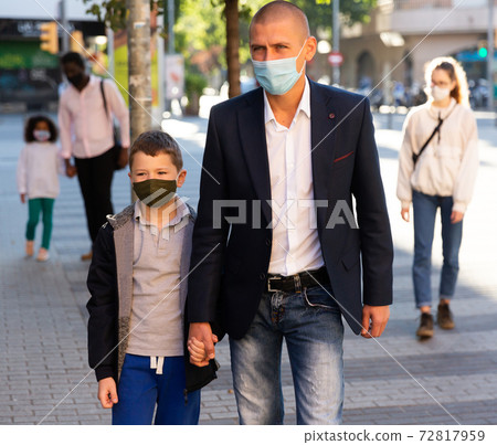 Man in face mask walking with preteen son along city street 72817959