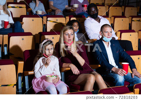 Parents with tween daughter in protective masks watching movie in cinema Parents with tween daughter in protective masks watching movie in cinema 72818203