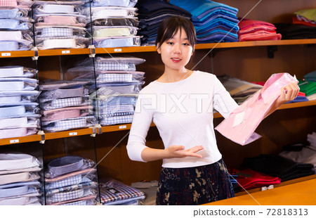 Glad female seller demonstrating shirts in mens clothes store 72818313