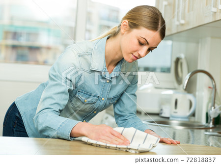 Positive housewife cleans the table in the kitchen 72818837