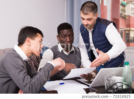 Serious men are talking about documents for project on laptop together Serious men are talking about documents for project on laptop together 72818925