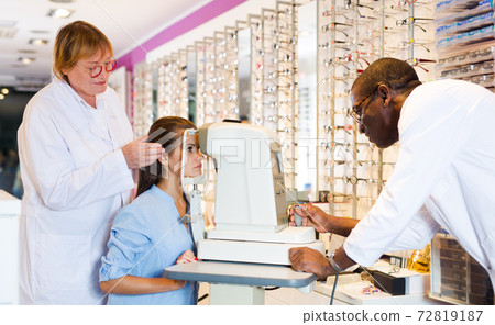 Two optometrists testing eyesight of woman 72819187
