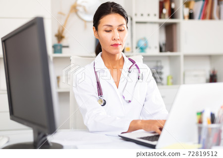 Kazhahstani female doctor in uniform is working behind laptop Kazhahstani female doctor in uniform is working behind laptop 72819512