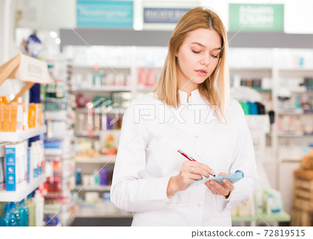 Pharmacist is writing down assortment of drugs in pharmacy 72819515