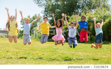 Happy school children jumping on the green lawn in park 72819674