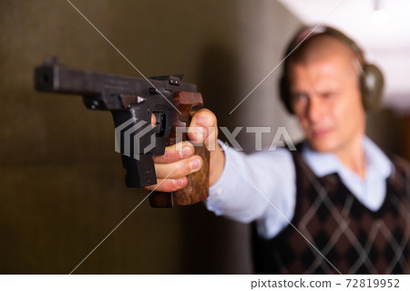Man with headphones shoots pistol at target in shooting range Man with headphones shoots pistol at target in shooting range 72819952